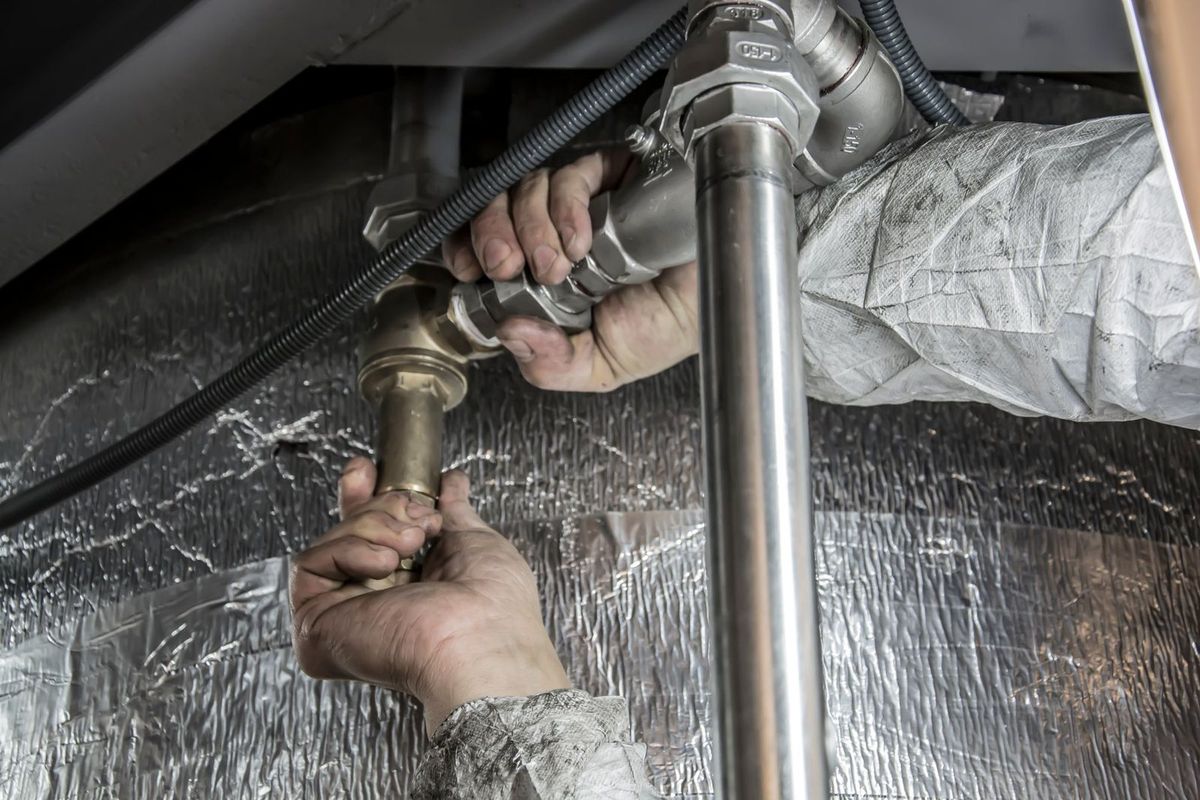 Hands repairing a pipe fitting under a sink