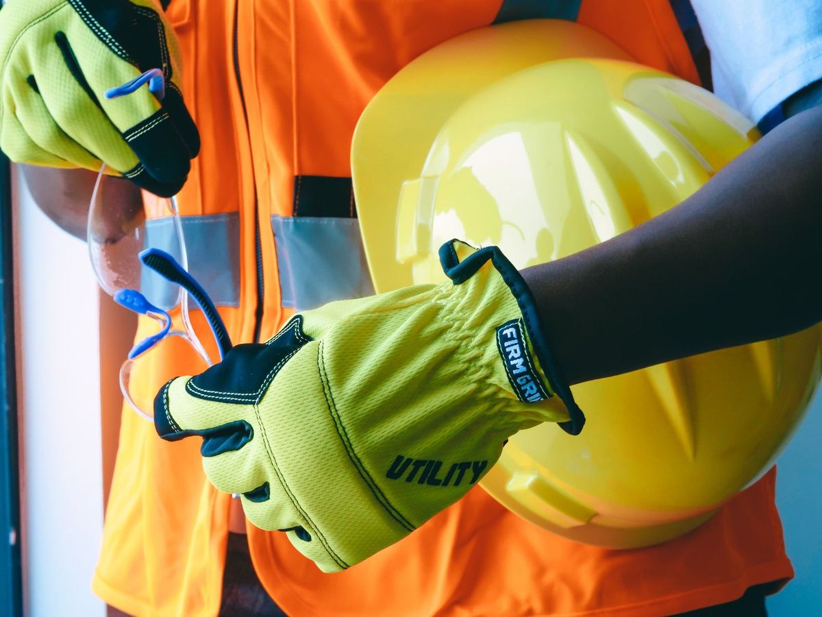 Technician pulling on work gloves and holding a hard hat